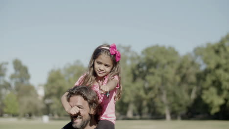 Cheerful-Caucasian-girl-sitting-on-dads-neck-during-walk-in-park